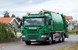 En grön återvinningsbil av märket Scania kör i ett villaområde.